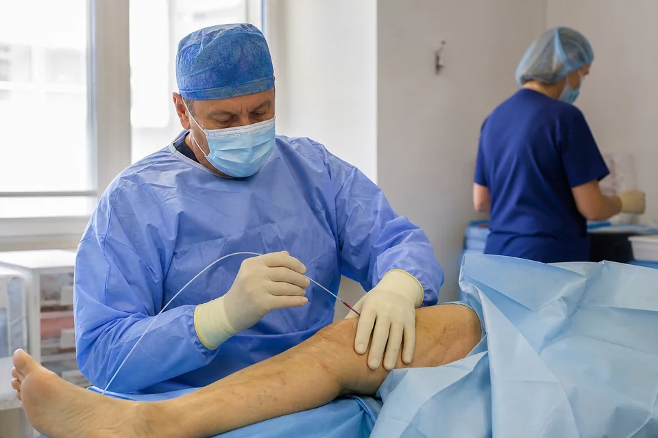 Chirurg naczyniowy przygotowuje cewnik do laserowego zamknięcia żyły na podudziu pacjenta w sali zabiegowej